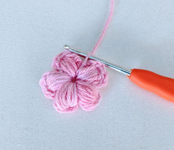 crochet pnk flower with 5 petals and a crochet hook on white background