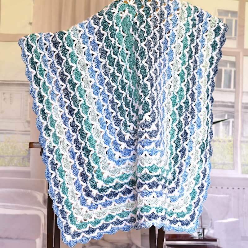 couverture au crochet bleu et blanc à motif coquillage suspendu au-dessus de la chaise