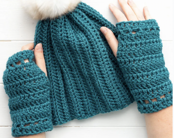 two hands on white background wearing teal coloured fingerless gloves with a hat in the middle