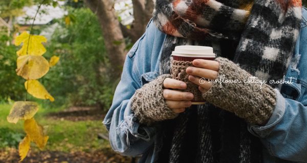 a woman holding a cup and wearing brown fingerless gloves and trees in the background