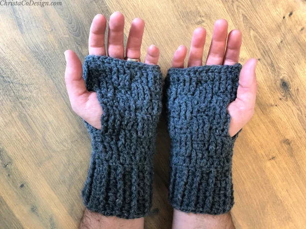 two hands wearing dark fingerless gloves on wooden background