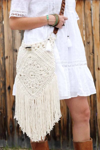 A woman in a white dress with a crochet crossbody bag featuring long tassels.