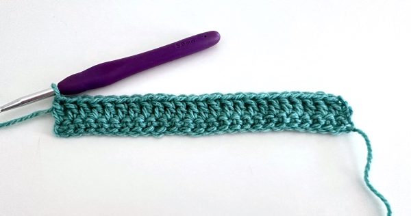 Second row completed using the double crochet stitches; green yarn, purple crochet hook on white background