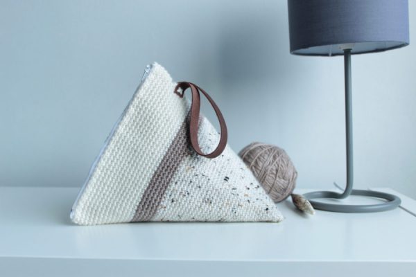 Small triangle-shaped crochet bag in white and brown on a white table.