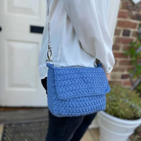 A person standing with a blue crocheted bag over their shoulder.
