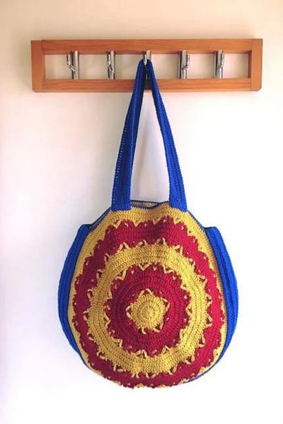 Bright blue, red, and yellow round crochet bag hanging on a wall hook.