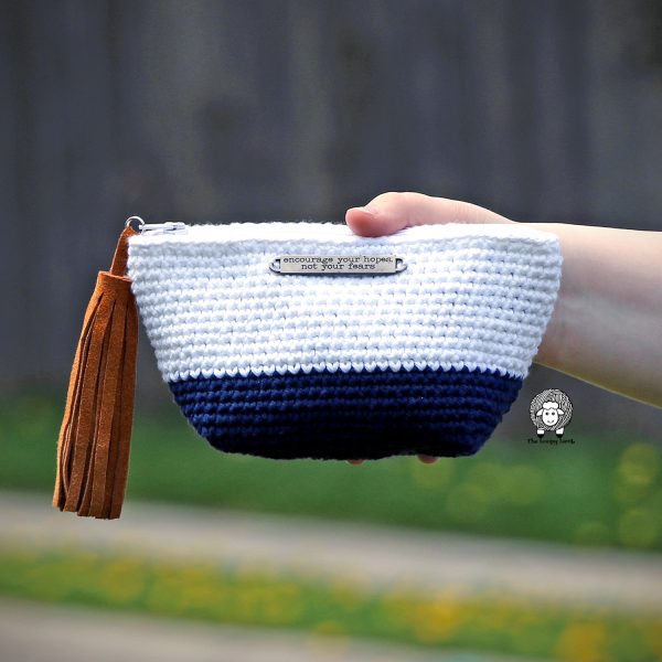 A hand holding a white and blue-colored crochet purse.