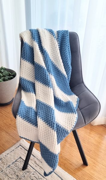 A modern crochet blanket with blue and white stripes, draped over a chair
