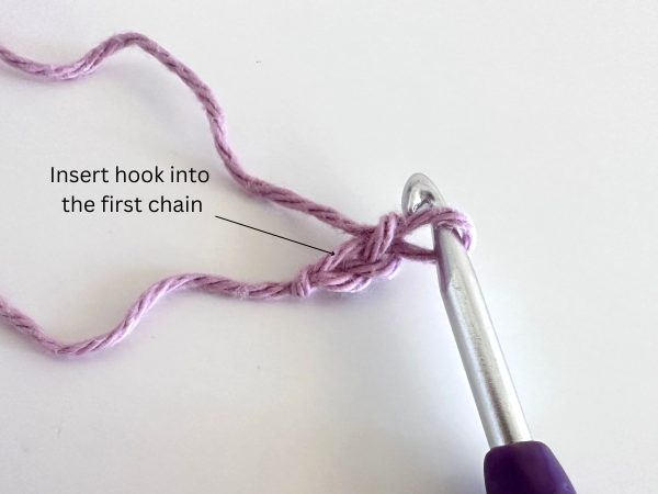 Two chained stitches in pink yarn with a purple hook, demonstrating the first step of the foundation single crochet stitch.