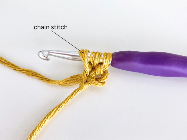 Three loops on a hook, using golden yellow yarn and a purple hook, demonstrating the second step of the foundation double crochet stitch