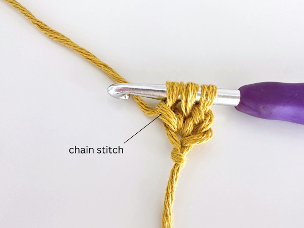Three loops on a hook, using golden yellow yarn and a purple hook, demonstrating the third step of the foundation double crochet stitch