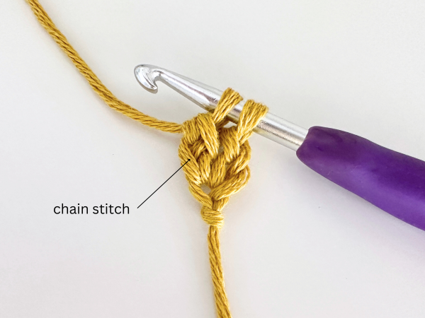 Two loops on a hook, using golden yellow yarn and a purple hook, demonstrating the fourth step of the foundation double crochet stitch