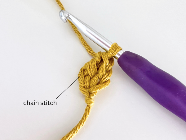 One loop on a hook, using golden yellow yarn and a purple hook, demonstrating the fourth step and the completion of the first foundation double crochet stitch