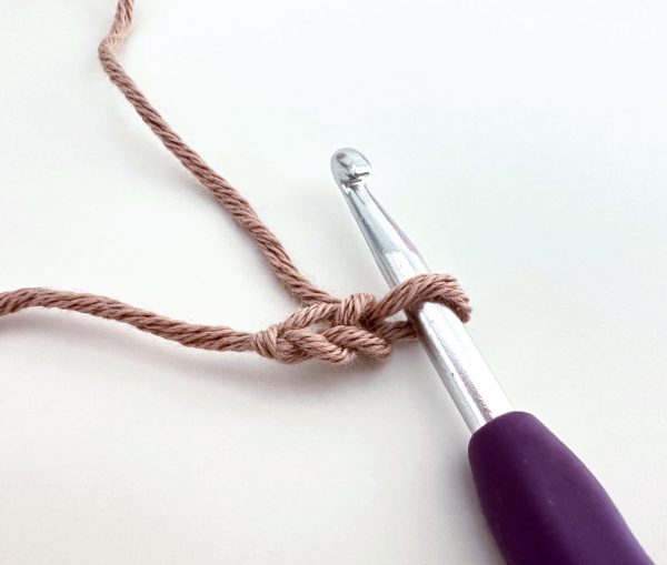 purple crochet hook and two chain stitches in light brown colour, on a white surface