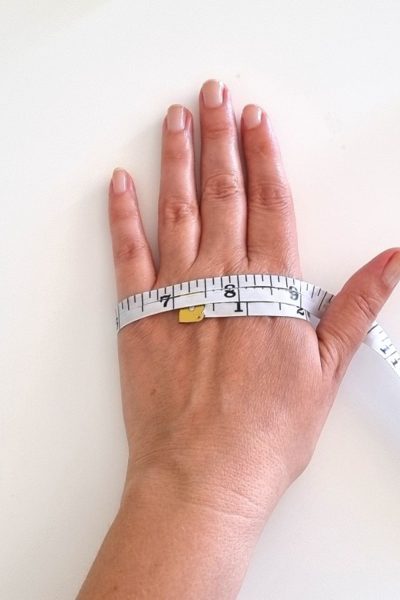 A left hand with a tape measure wrapped around it, indicating a width of 7 inches.