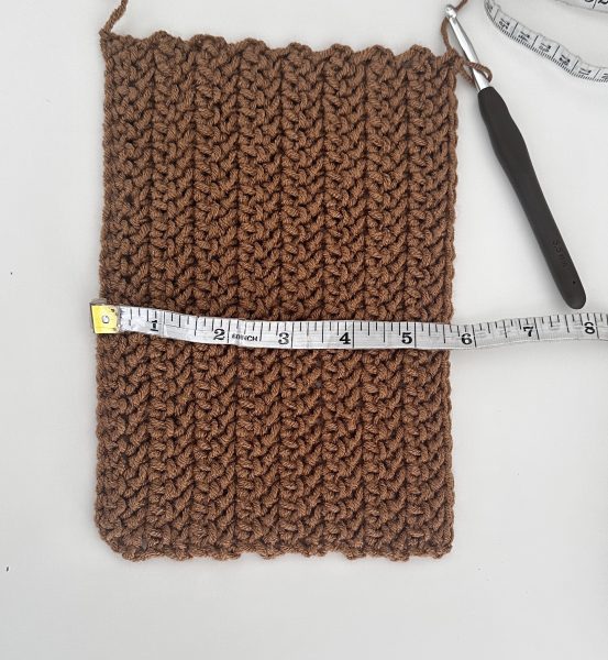 crocheted rectangle in brown yarn colour with a tape measure on top, indicating a width of 5.5 inches.